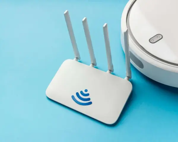 Un router Wi-Fi bianco con logo blu e un robot aspirapolvere bianco su sfondo azzurro. Cos'è un router? È il cuore della tua connessione internet.