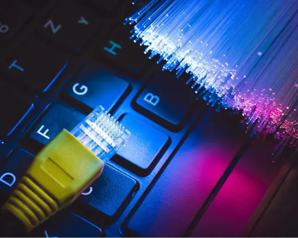 Connessione internet: un cavo giallo su tastiera e fibre ottiche luminose. Capire cos'è l'ADSL è fondamentale per la tua navigazione.