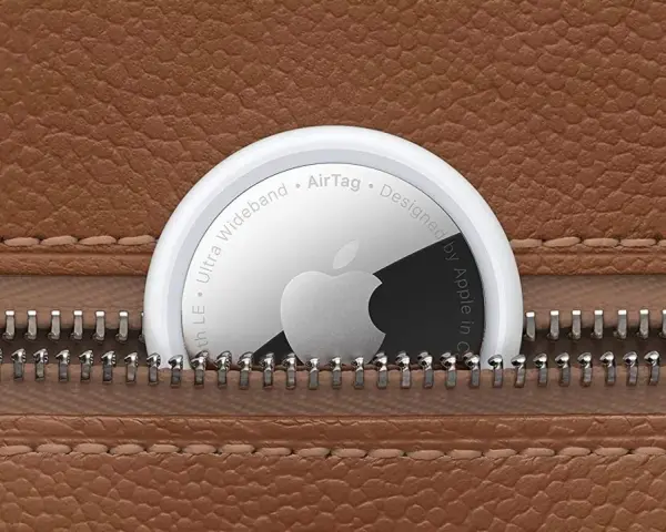 Un AirTag Apple sporge da una cerniera di una borsa in pelle marrone. Scopri airtag come funziona per ritrovare i tuoi oggetti.