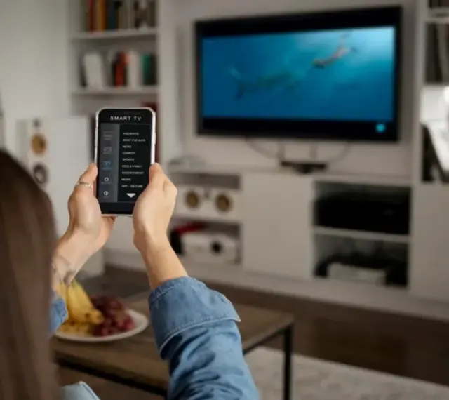 Una persona usa il suo smartphone per controllare la Smart TV, mostrando come collegare il telefono alla tv per un'esperienza di intrattenimento domestico.