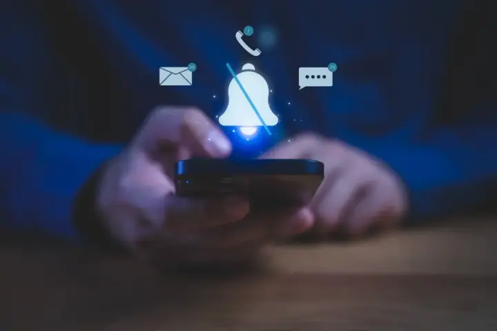 Mani che tengono uno smartphone, con icone di notifiche (email, messaggi, chiamate) e una campana barrata, per illustrare come silenziare le notifiche.