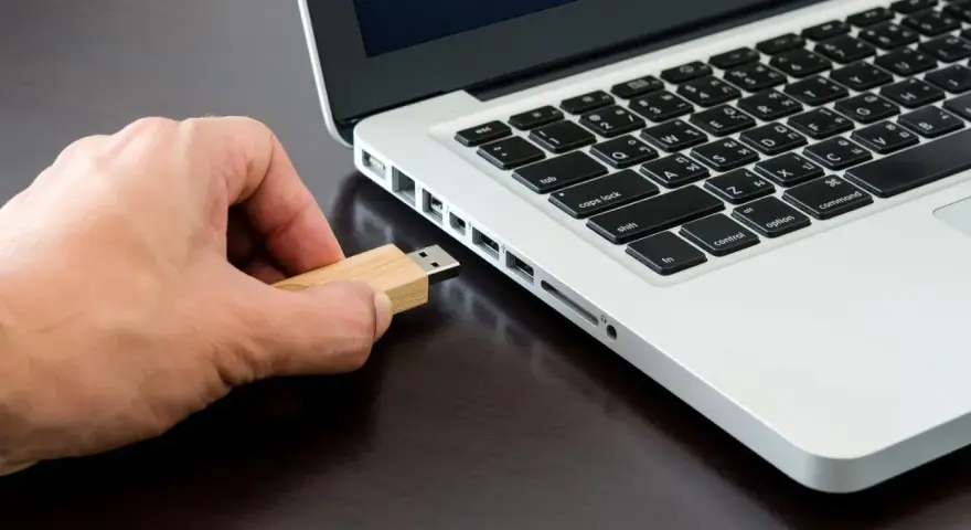 Mano inserisce una chiavetta USB in un laptop, pronta per formattare.