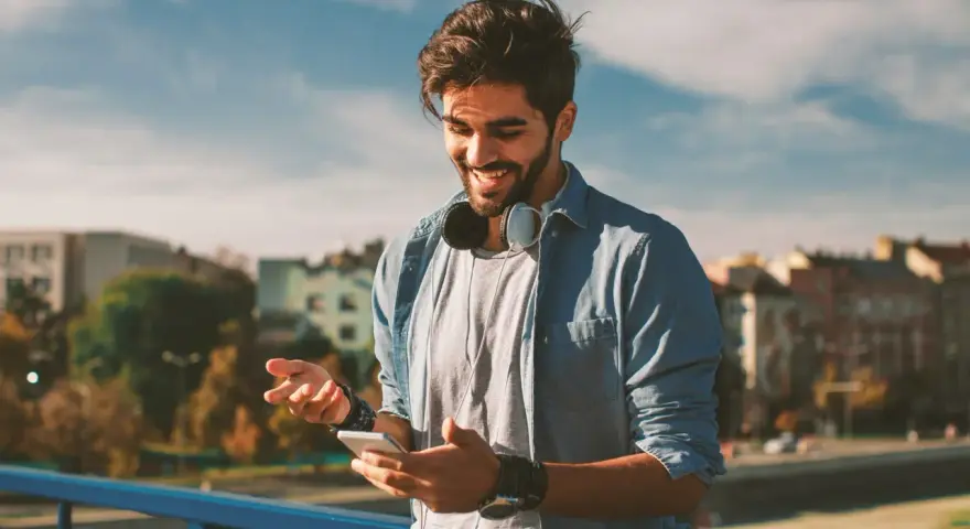 Giovane sorridente con smartphone e cuffie, impara come telefonare dall'estero in Italia con il cellulare.