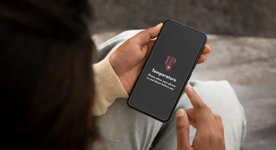 Mani che tengono uno smartphone con un messaggio di avviso "Temperatura". È ora di capire come raffreddare il telefono.