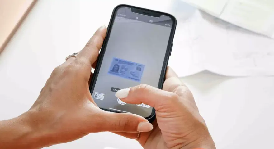 Mani che usano uno smartphone per scannerizzare un documento d'identità. L'app mostra un'anteprima del documento.