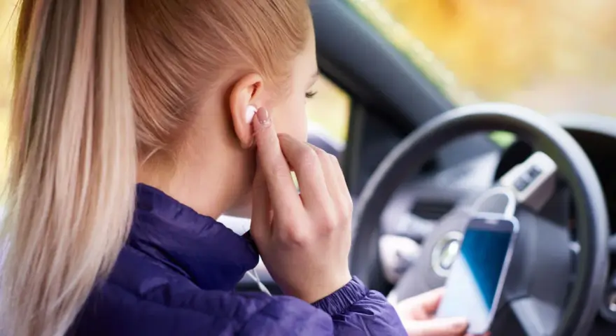 Ragazza in auto inserisce auricolari, pronta per ascoltare musica o chiamare. Come togliere la e sul cellulare? Forse sta cercando un modo per disattivare le notifiche.