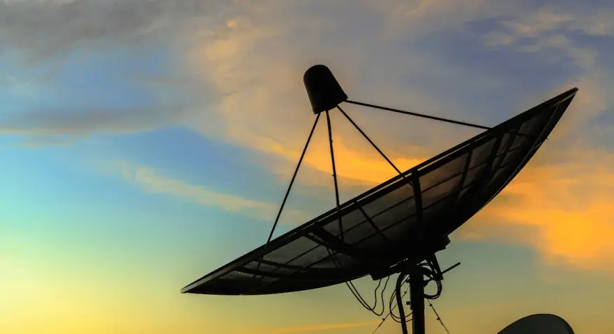 Antenna parabolica in controluce al tramonto, pronta a connettersi al mondo tramite internet satellitare.