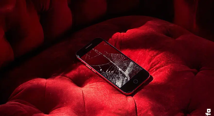 Telefono con schermo rotto su un divano rosso. Non riesco a spegnere il telefono, è bloccato.