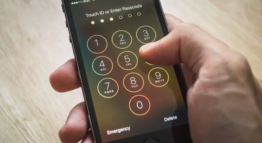 Dito si vede come sbloccare iPhone inserendo il codice. La mano preme i tasti numerici sullo schermo.