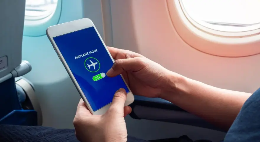 Mani che attivano la modalità aereo sul telefono, seduti vicino al finestrino di un aereo.
