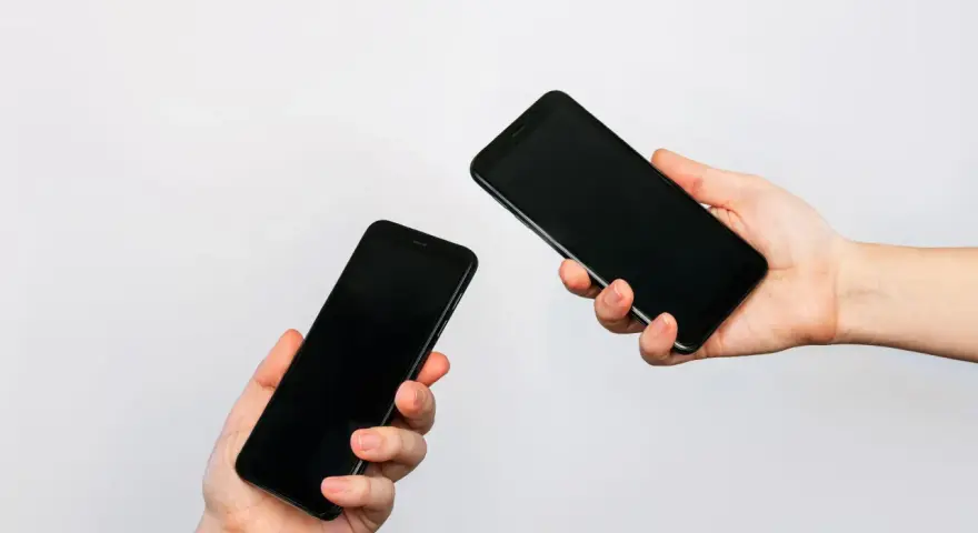 Due mani tengono due smartphone neri, uno in primo piano e uno più lontano, illustrando come trasferire i dati da un telefono all'altro.