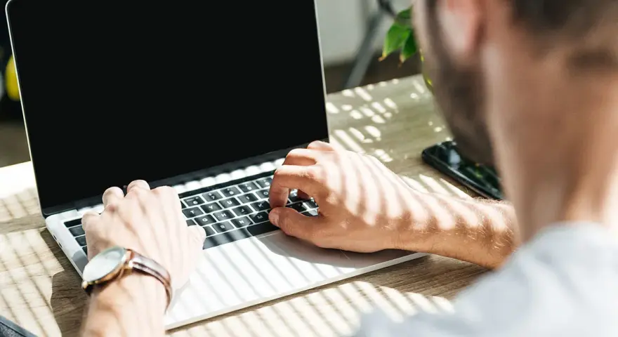 Uomo al lavoro su un laptop, monitora la temperatura CPU. Luce solare filtra attraverso le persiane.