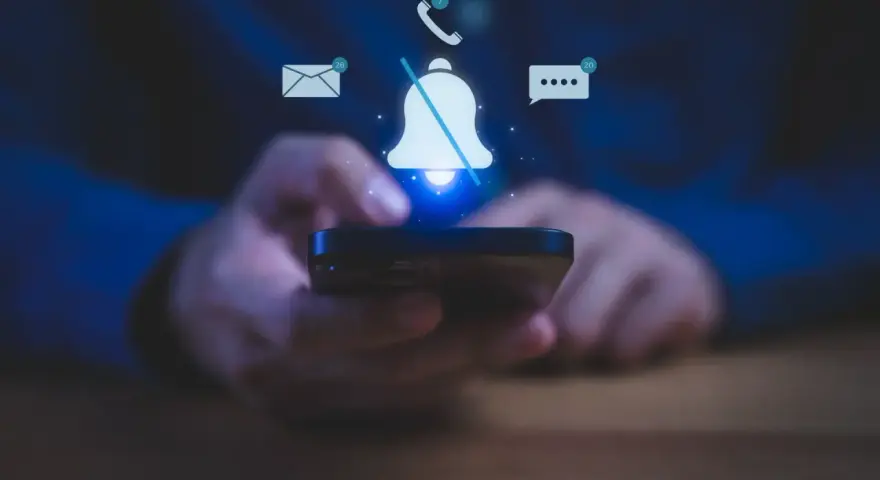 Mani che tengono uno smartphone, con icone di notifiche (email, messaggi, chiamate) e una campana barrata, per illustrare come silenziare le notifiche.