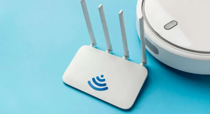 Un router Wi-Fi bianco con logo blu e un robot aspirapolvere bianco su sfondo azzurro. Cos'è un router? È il cuore della tua connessione internet.