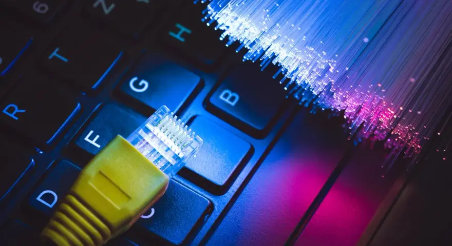 Connessione internet: un cavo giallo su tastiera e fibre ottiche luminose. Capire cos'è l'ADSL è fondamentale per la tua navigazione.