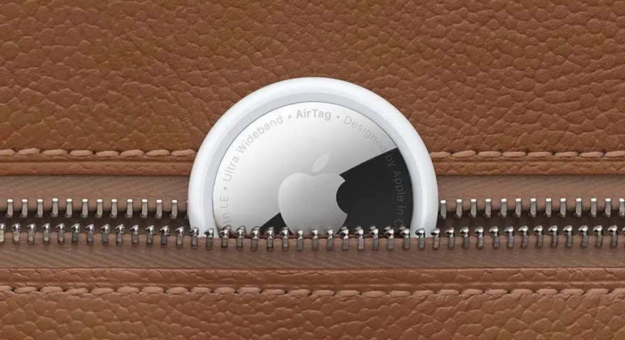 Un AirTag Apple sporge da una cerniera di una borsa in pelle marrone. Scopri airtag come funziona per ritrovare i tuoi oggetti.