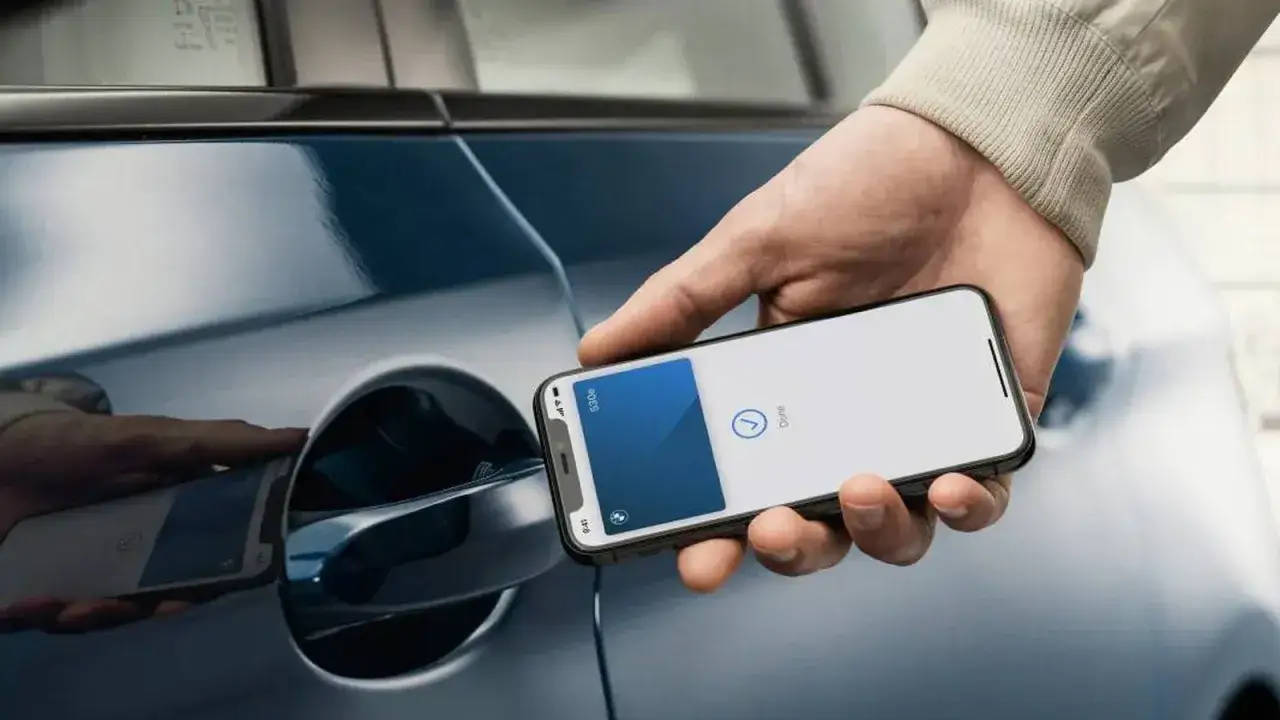 Un iPhone con tecnologia NFC si avvicina alla maniglia di un'auto blu per sbloccarla.