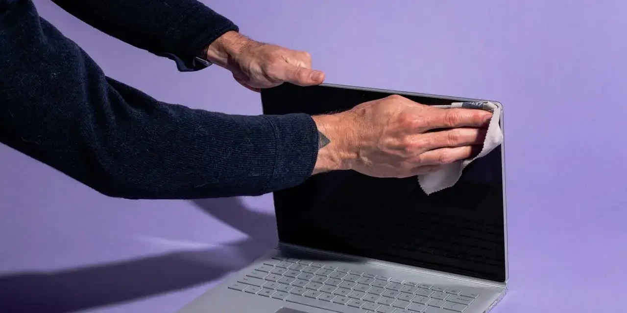 Mani che puliscono lo schermo del PC con un panno in microfibra per rimuovere impronte e polvere, garantendo una visione nitida.