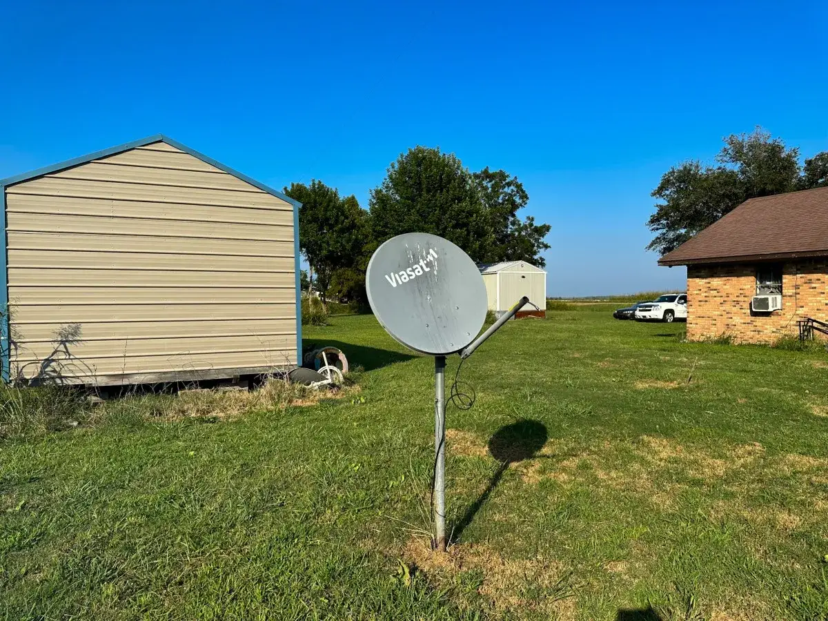 Un'antenna parabolica Viasat, essenziale per l'internet satellitare, punta verso il cielo azzurro, con un capannone e una casa sullo sfondo.
