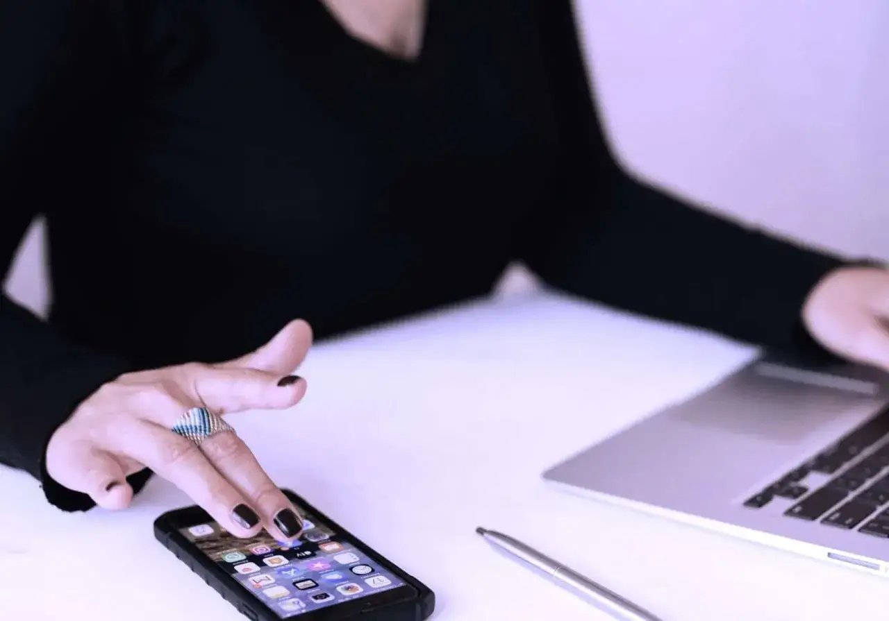 Mano con anello tocca smartphone, imparando come silenziare le notifiche per concentrarsi sul lavoro al laptop.