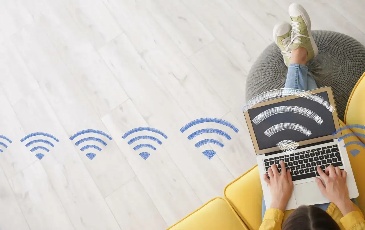 Persona che usa un laptop su un divano giallo, con icone Wi-Fi disegnate che si estendono sulla stanza. La connessione &egrave; forte, come un fwa 1gb.
