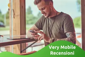 Uomo con tatuaggi guarda il suo smartphone, leggendo le very opinioni su "Very Mobile Recensioni".